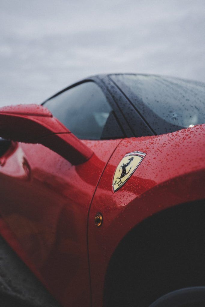 Red Ferrari sports car with rain droplets on its side, featuring the Ferrari emblem.