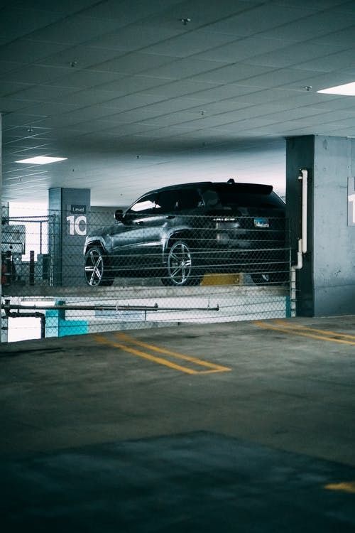 SUV parked in a dimly lit parking garage with yellow lines and a chain link fence.