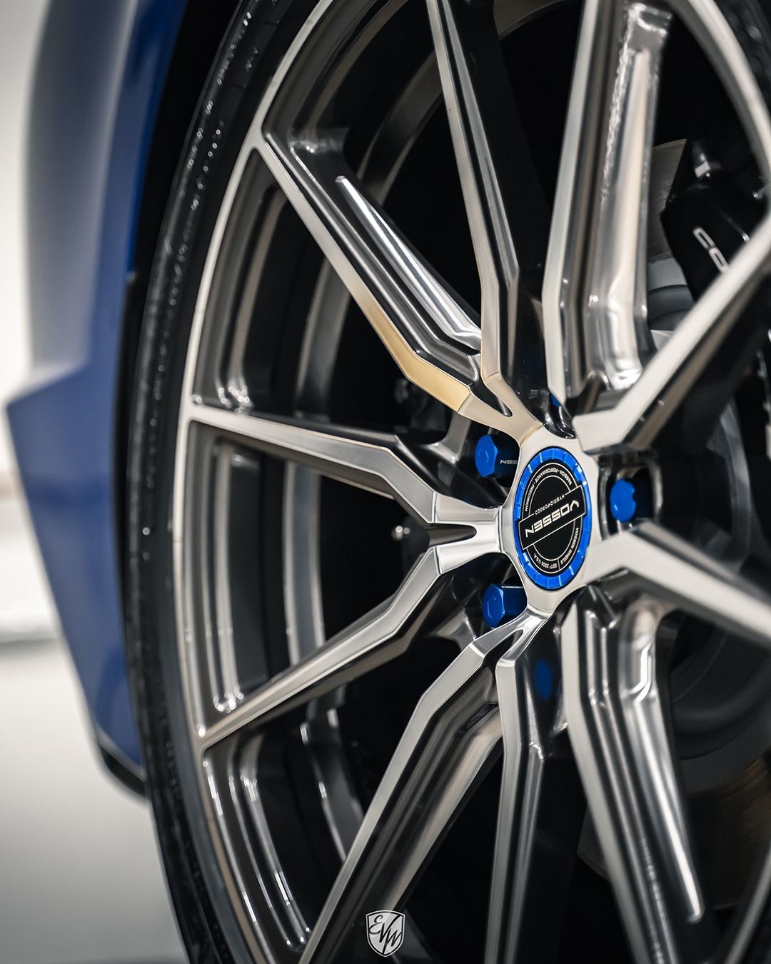 Close-up of a car wheel with silver and dark gray spokes, blue lug nuts, and a blue center cap.