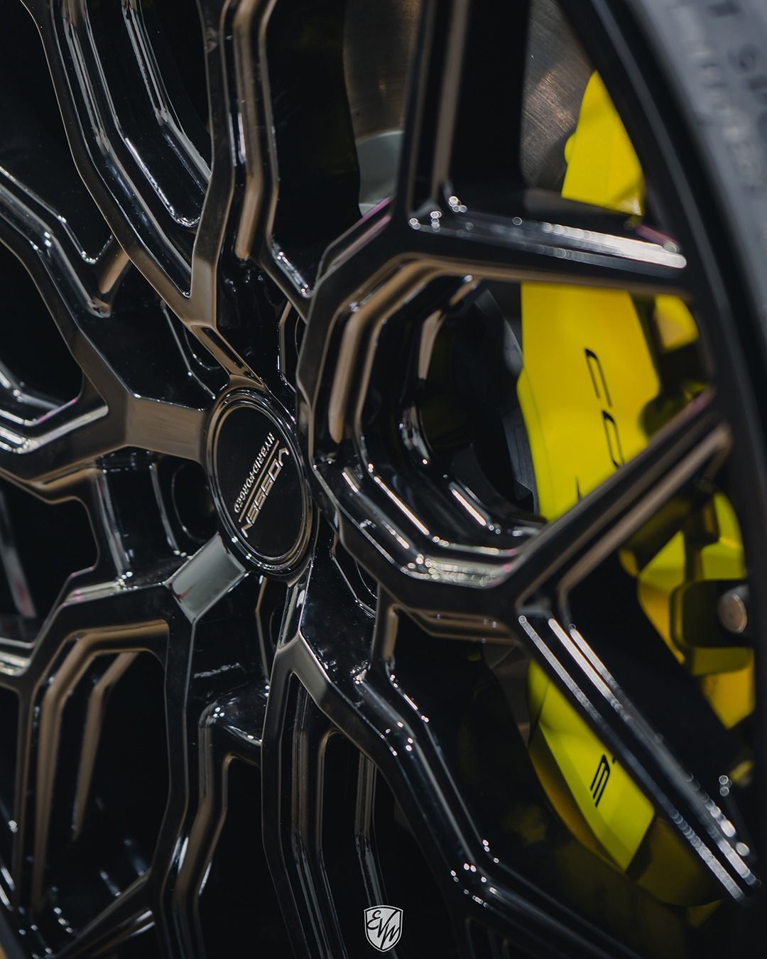 Black car wheel with a complex geometric design, bright yellow brake caliper visible behind the spokes.