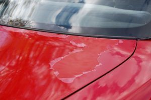 Red car paint peeling near windshield.