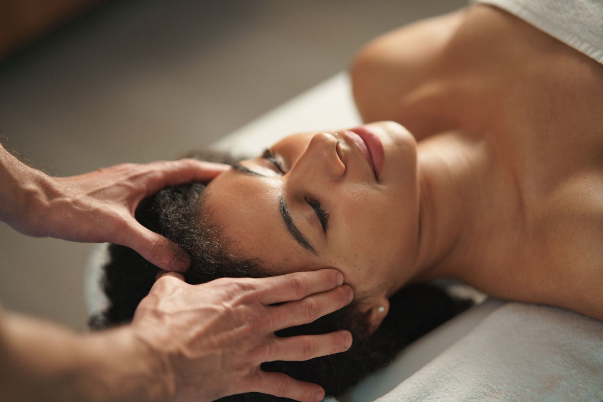Woman receiving a scalp massage with hands on her head, eyes closed, lying on a spa bed.