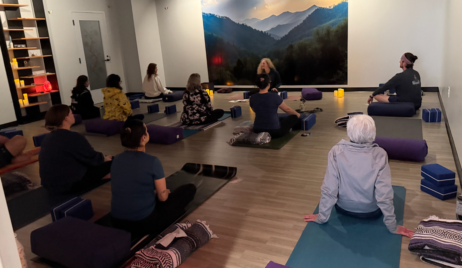 Yoga class: women smiling, hands in prayer pose, indoors with others.