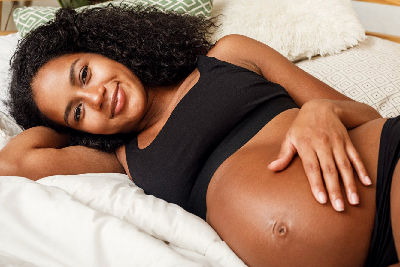 Pregnant Black woman lying on bed, smiling and touching her belly.