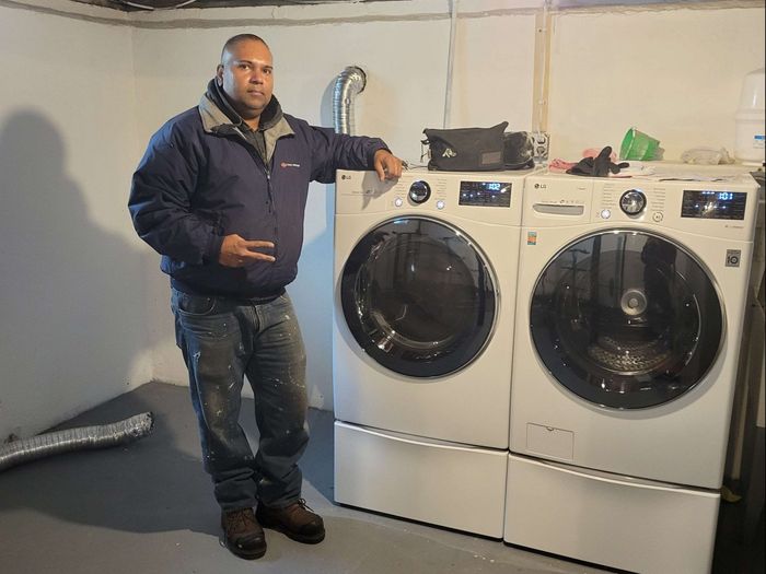 Repairman kneeling next to a washing machine and looking at camera isolated on white background