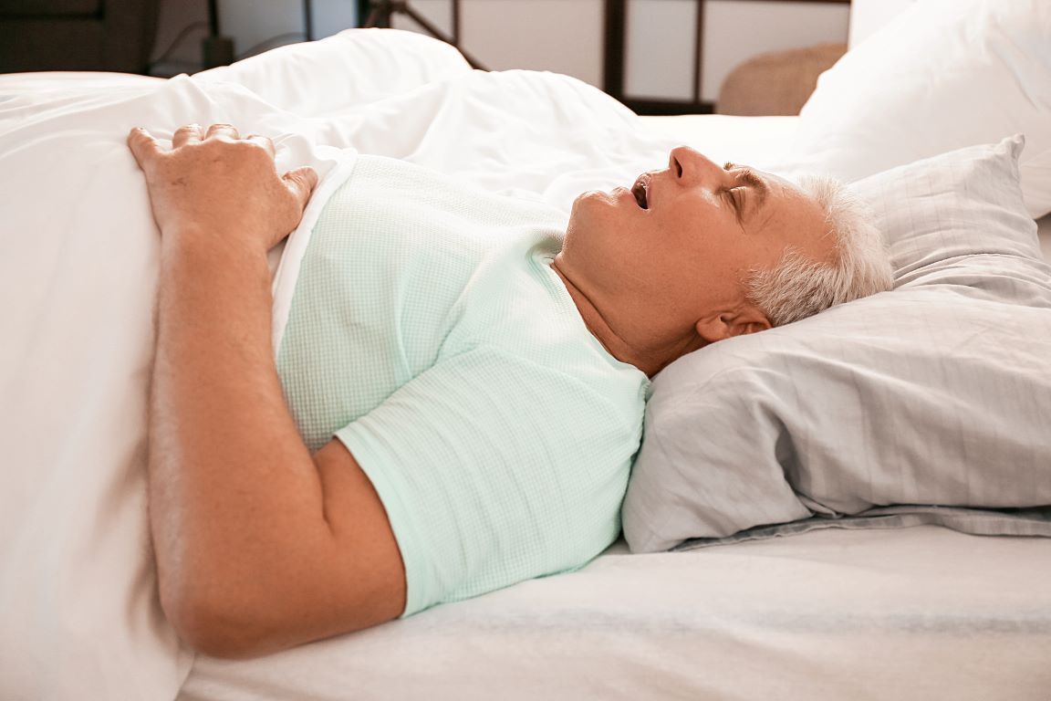 An elderly man is sleeping on a bed with his mouth open near Wake Forest, NC.