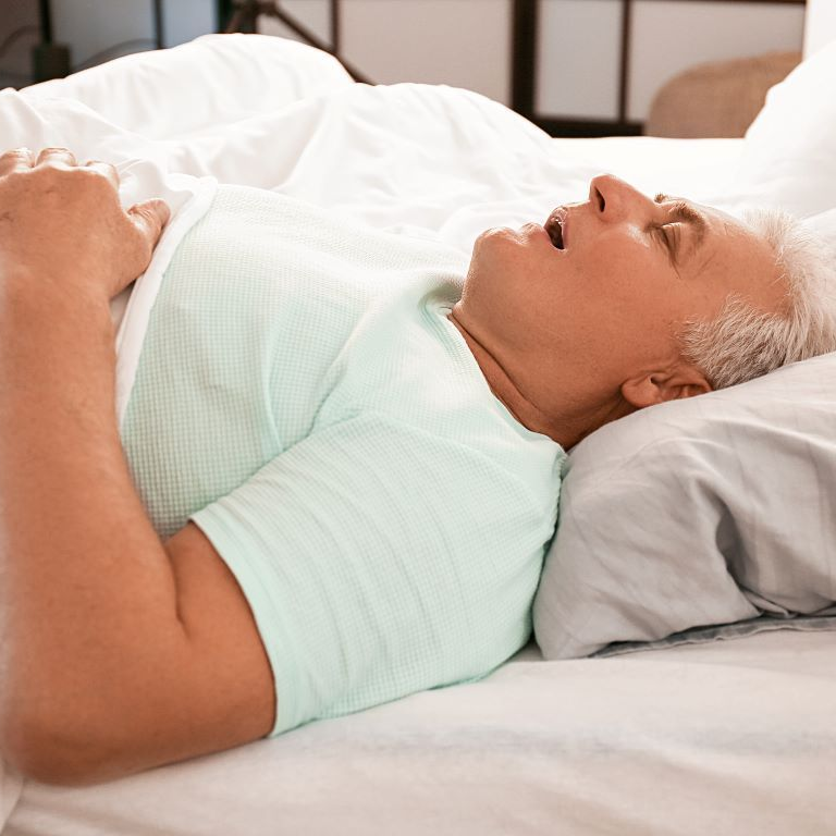 An elderly man is sleeping on a bed with his mouth open near Garner, NC.
