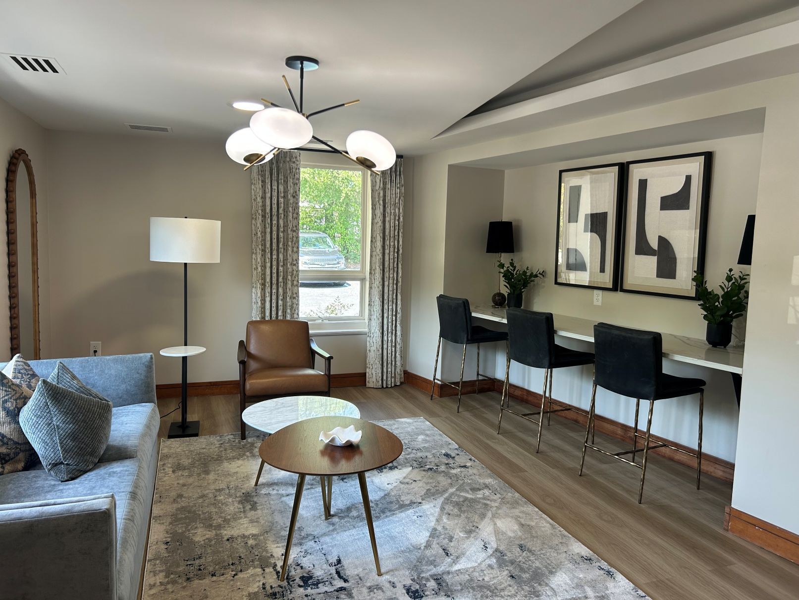 Bright living room with gray sofa, floor lamp, armchair, coffee table, and wall art beside a desk area near Wake Forest NC.