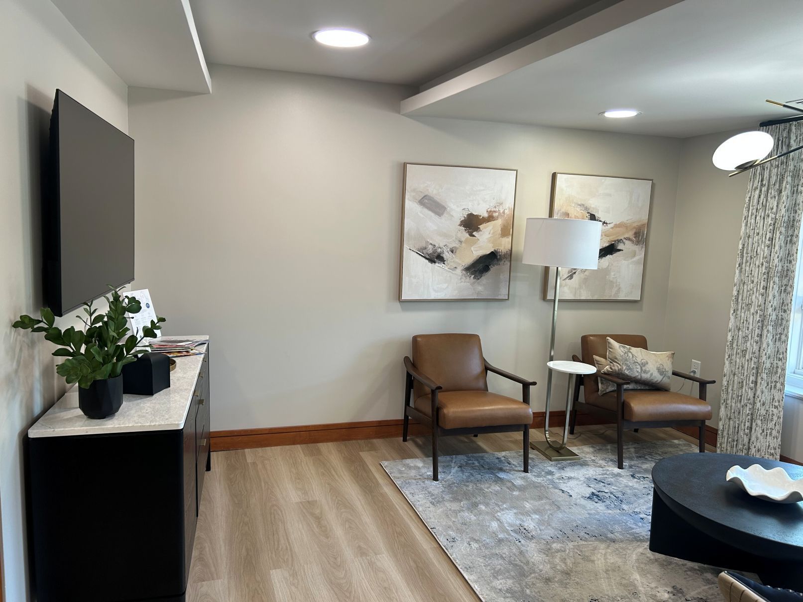 Modern living room with gray walls, brown chair, abstract art, TV, lamp, and patterned curtains in Raleigh NC
