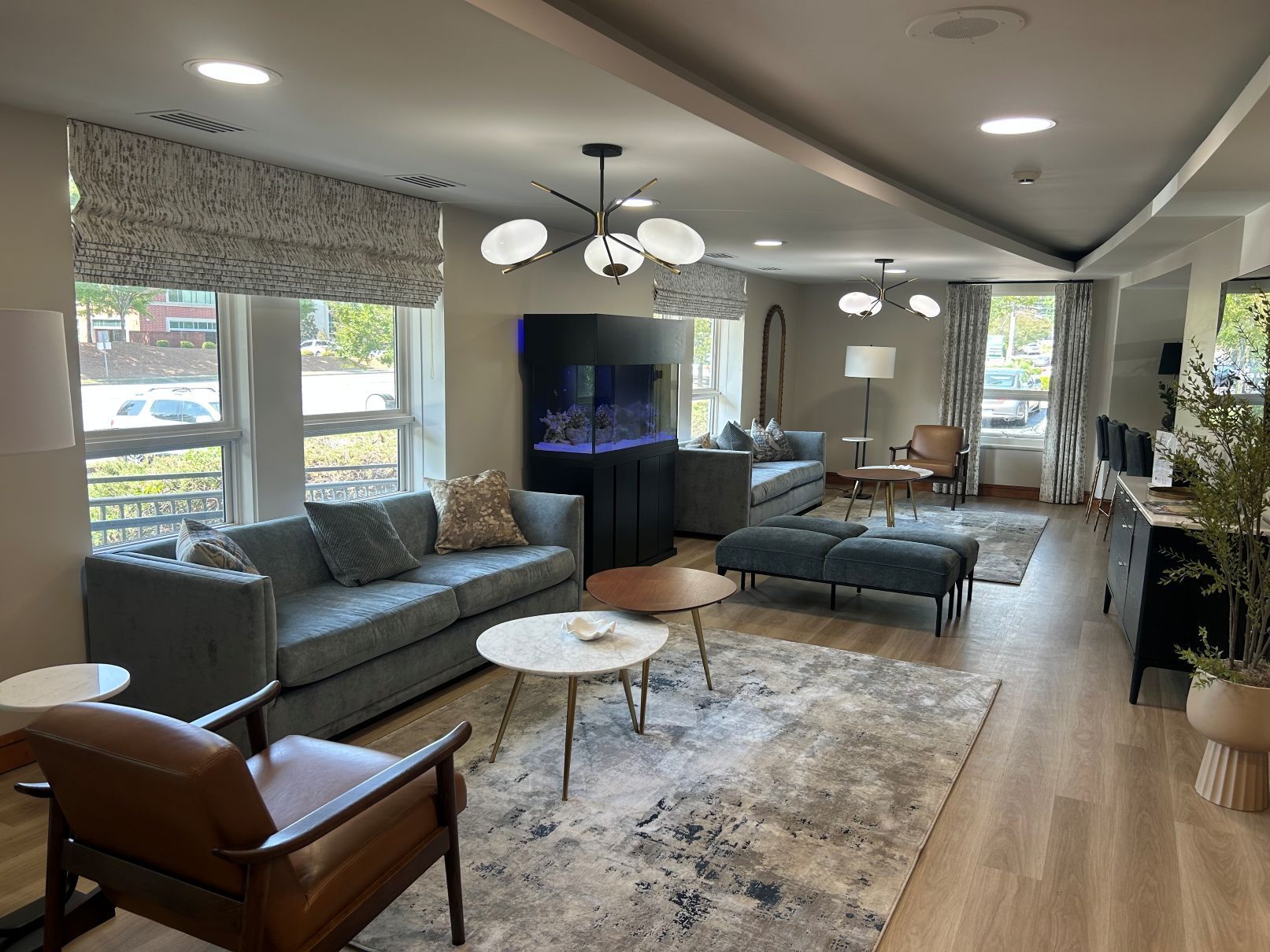Modern living room with gray sofas, a brown chair, TV, coffee table, and large windows in Raleigh NC.