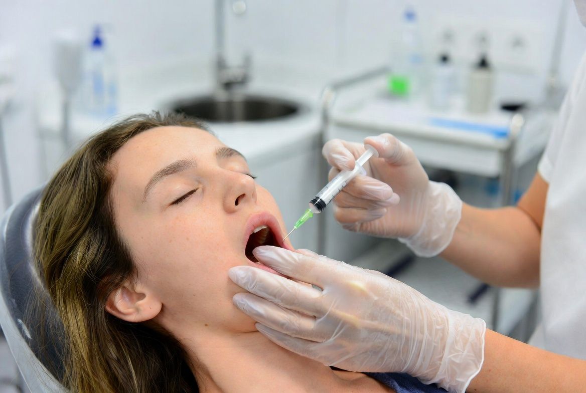 Dentist numbing a patient’s mouth with a syringe in a clinic, wearing gloves and mask in Raleigh, NC.