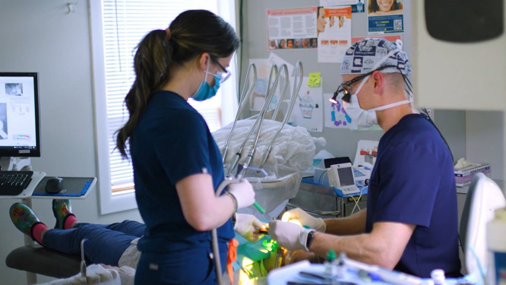 A dentist and a nurse are working on a patient 's teeth in a dental office.