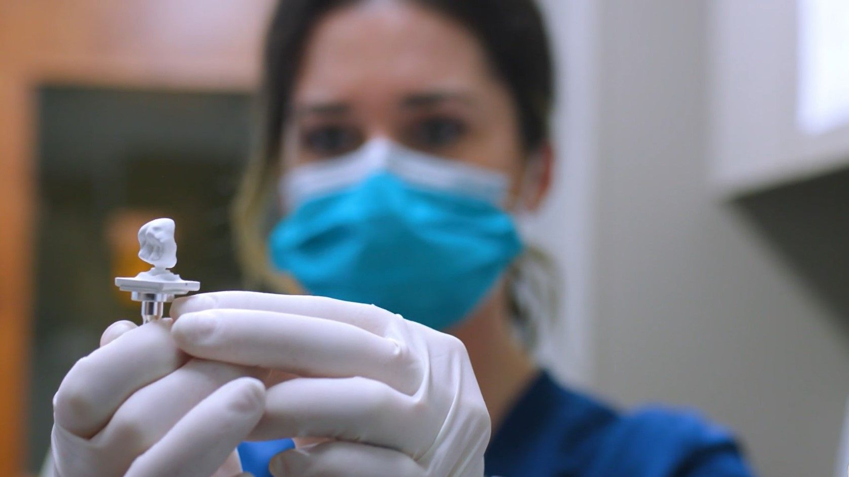 A nurse wearing a mask and gloves is holding a small object in her hands.