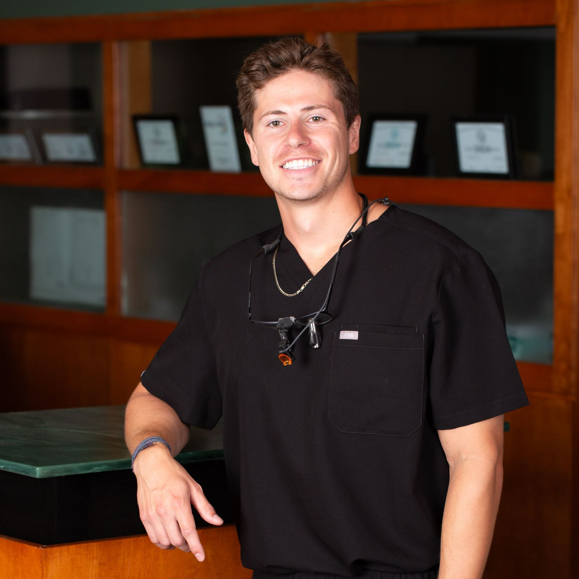 A smiling man wearing a black scrub top is standing in front of a counter