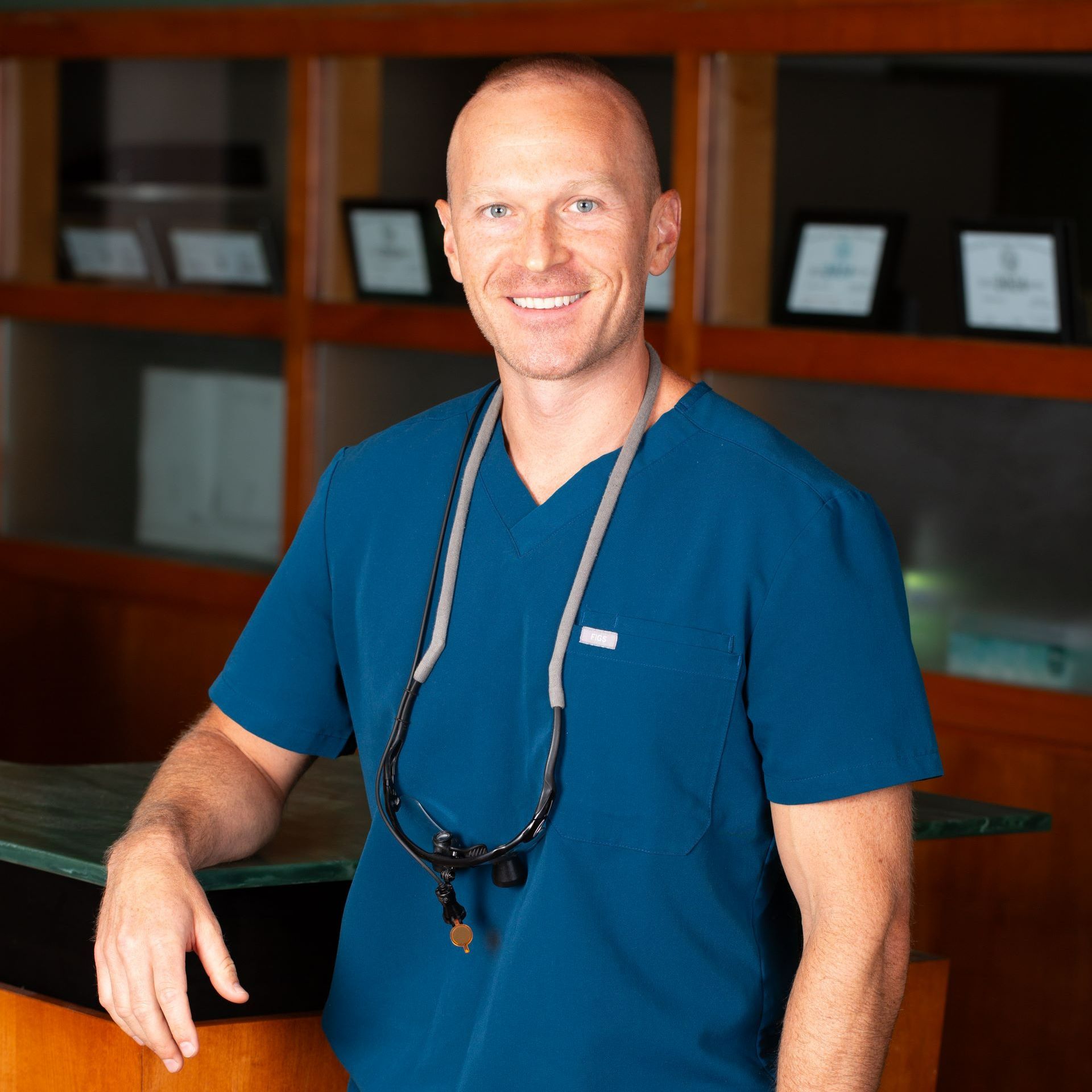 A man in a blue scrub top with a stethoscope around his neck