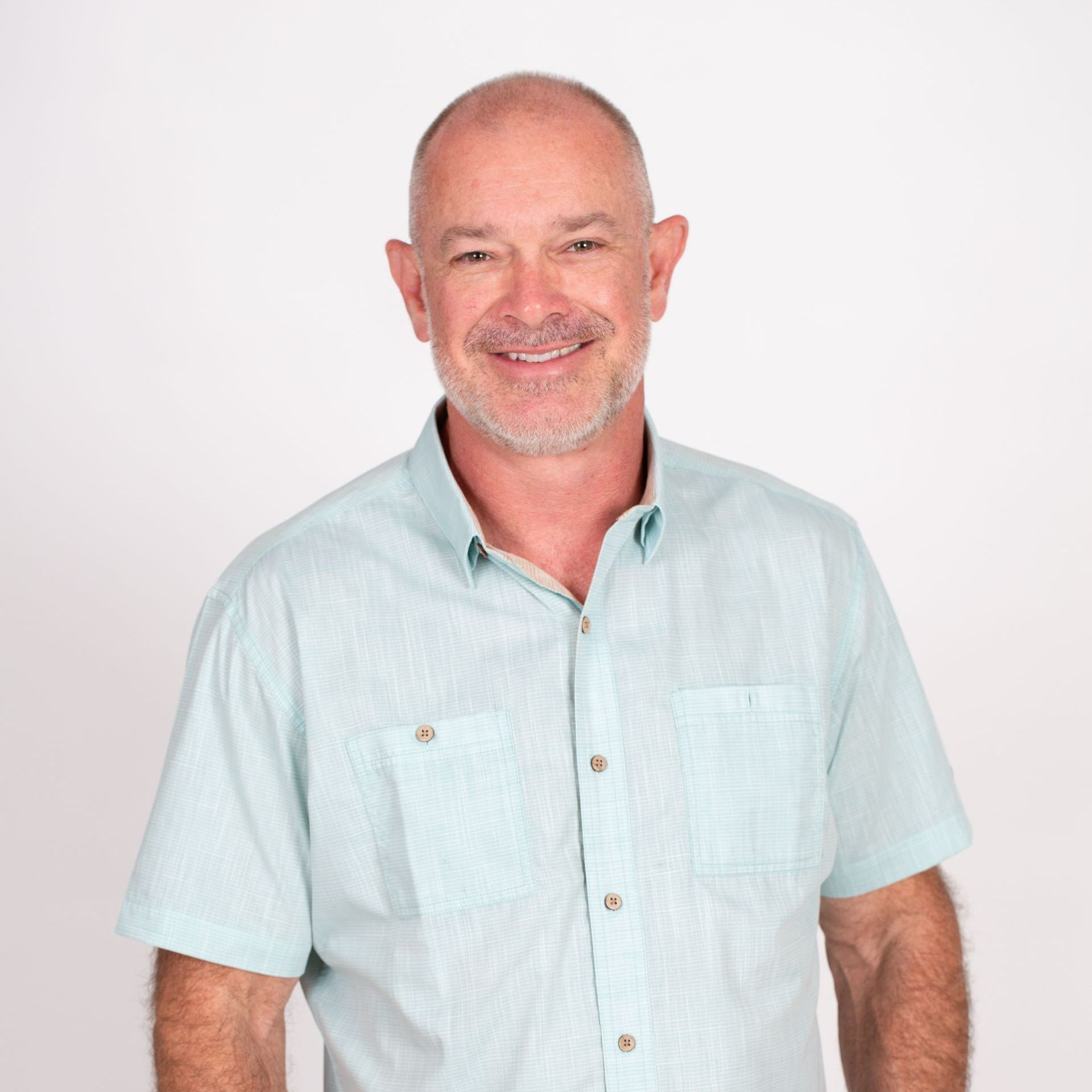 A man with a beard is wearing a light blue shirt and smiling.