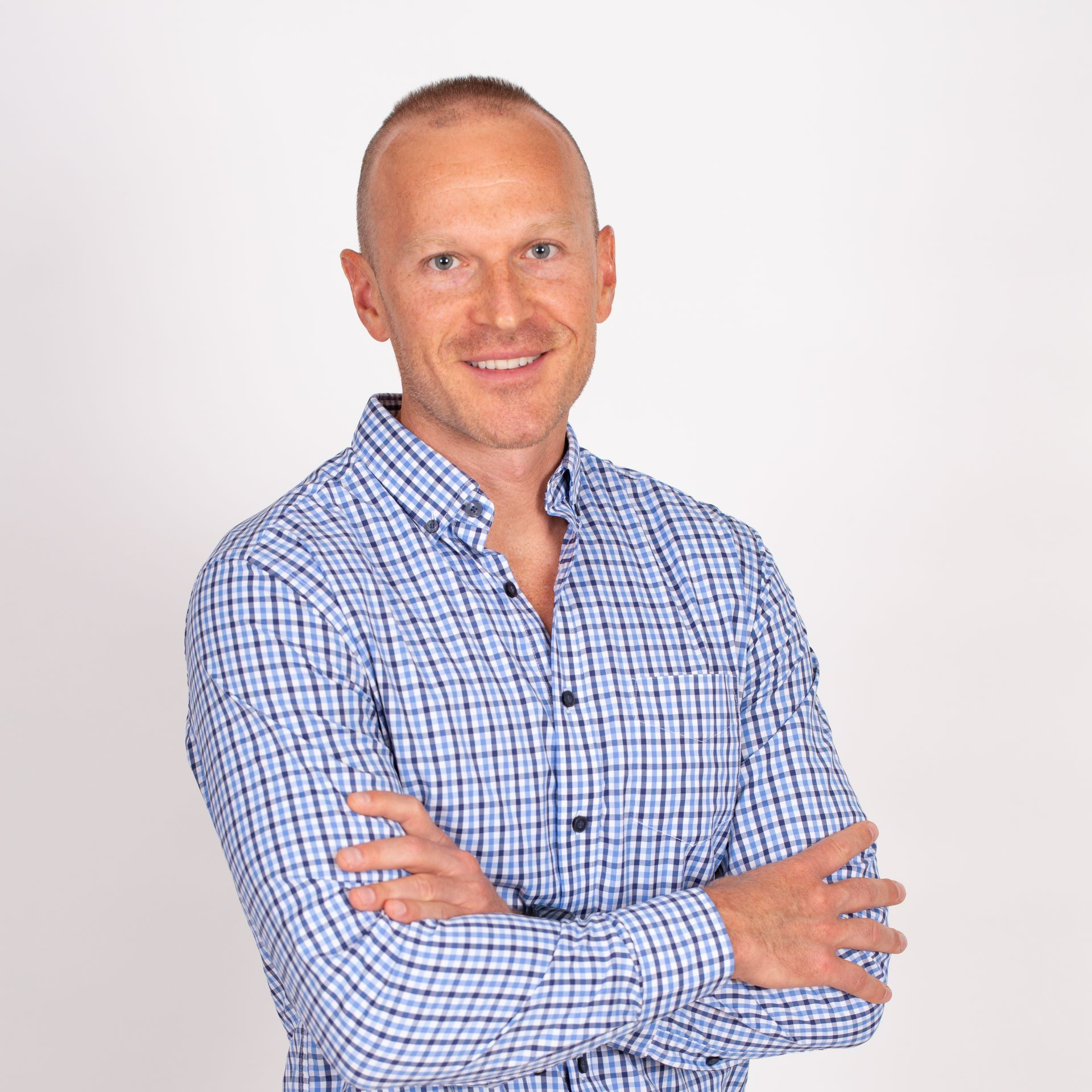 A man in a blue plaid shirt is standing with his arms crossed and smiling.