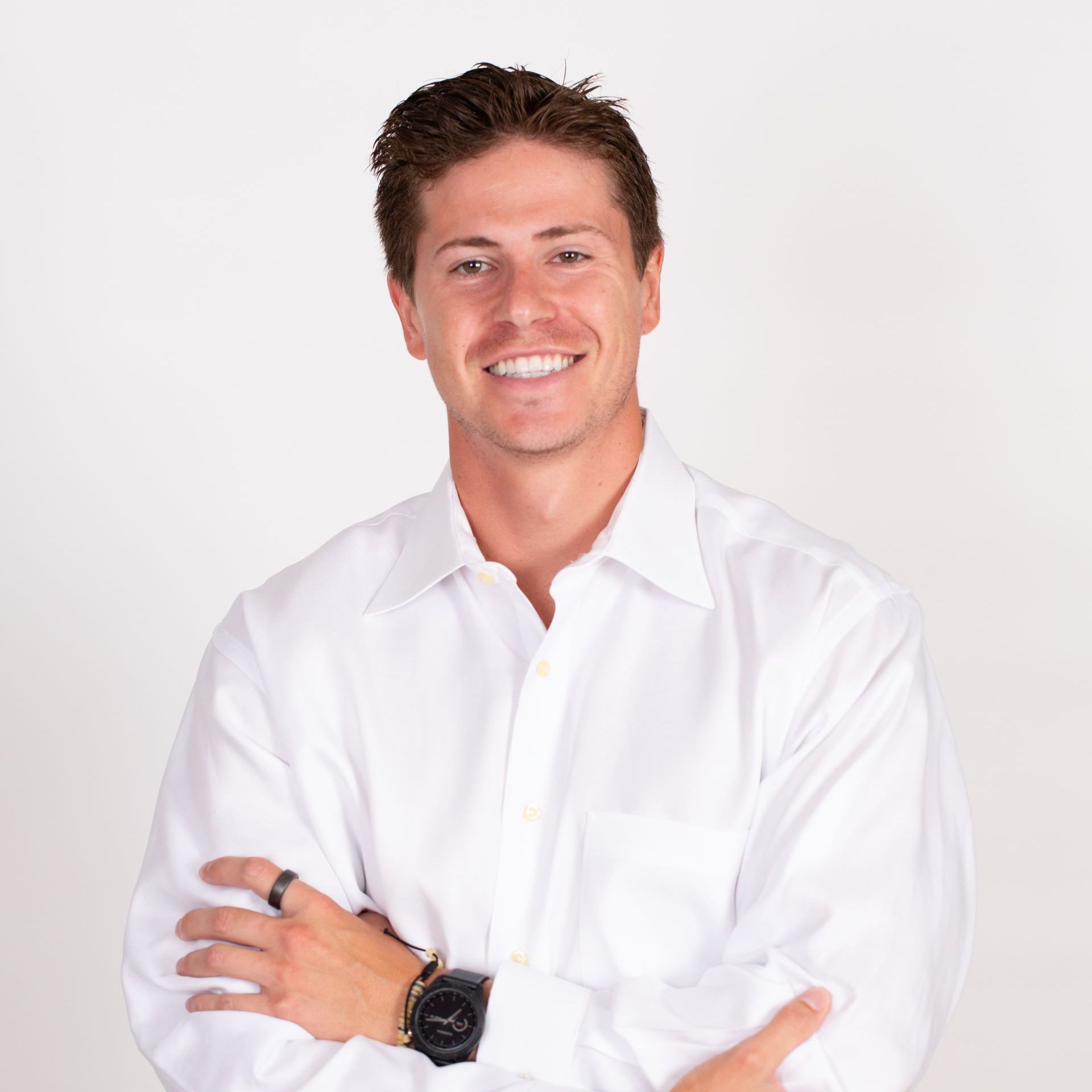 A man in a white shirt is smiling with his arms crossed