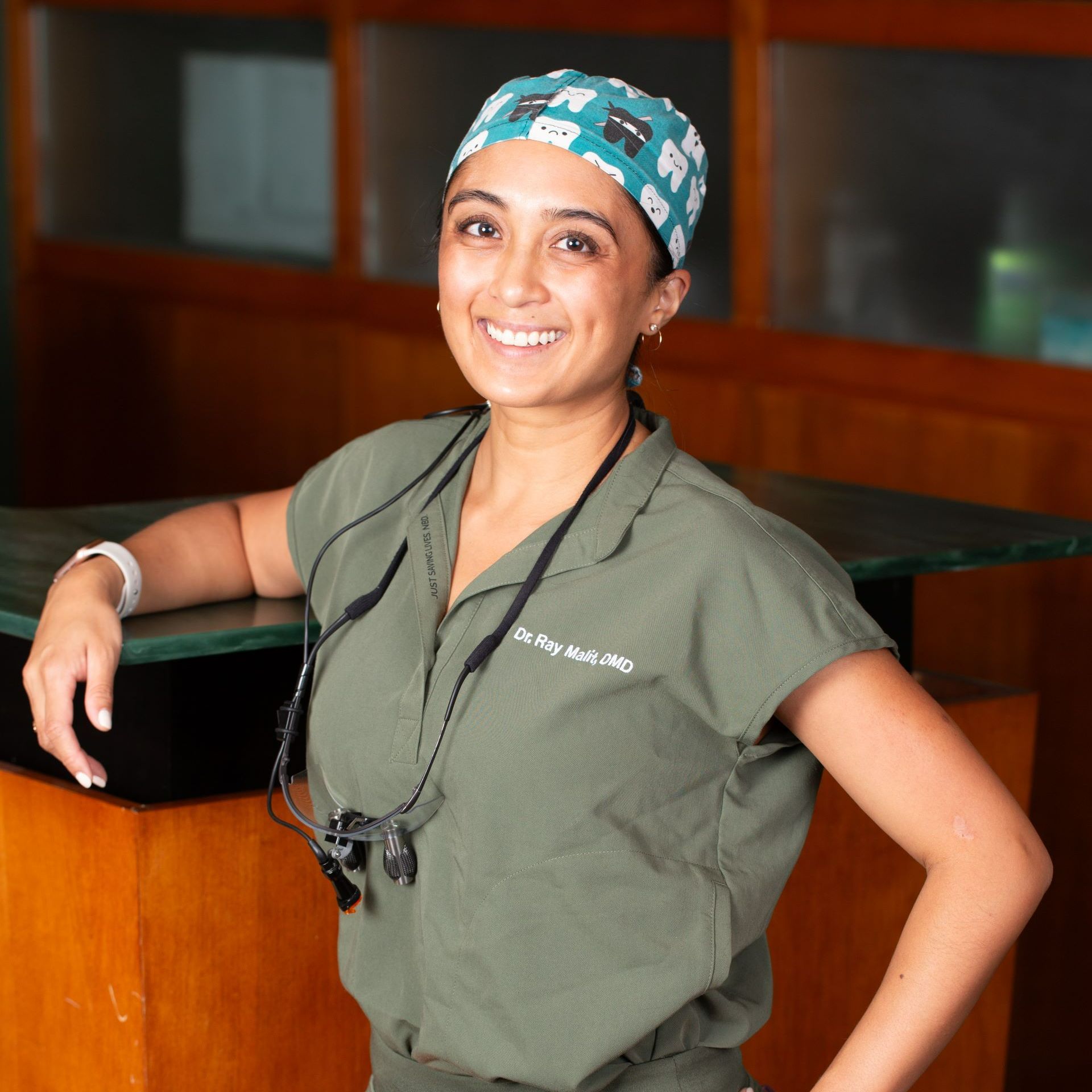 A female doctor wearing a green scrub top and a blue hat