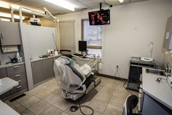 A dental office with a dental chair and a monitor hanging from the ceiling.