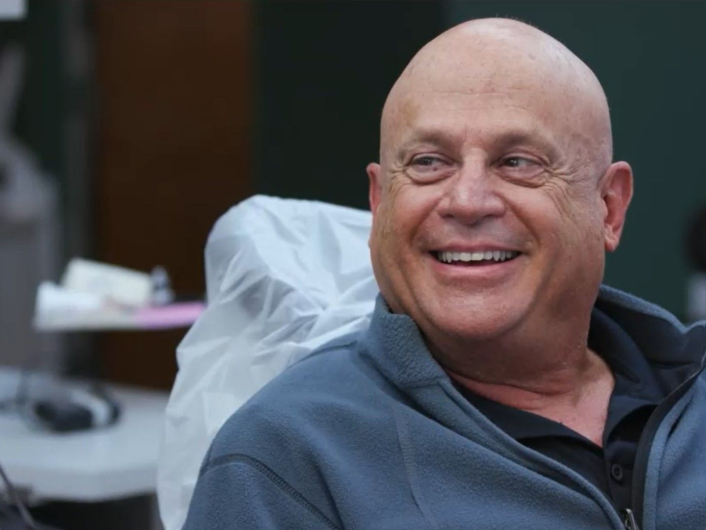 A female dentist is talking to a bald man in a dental chair.