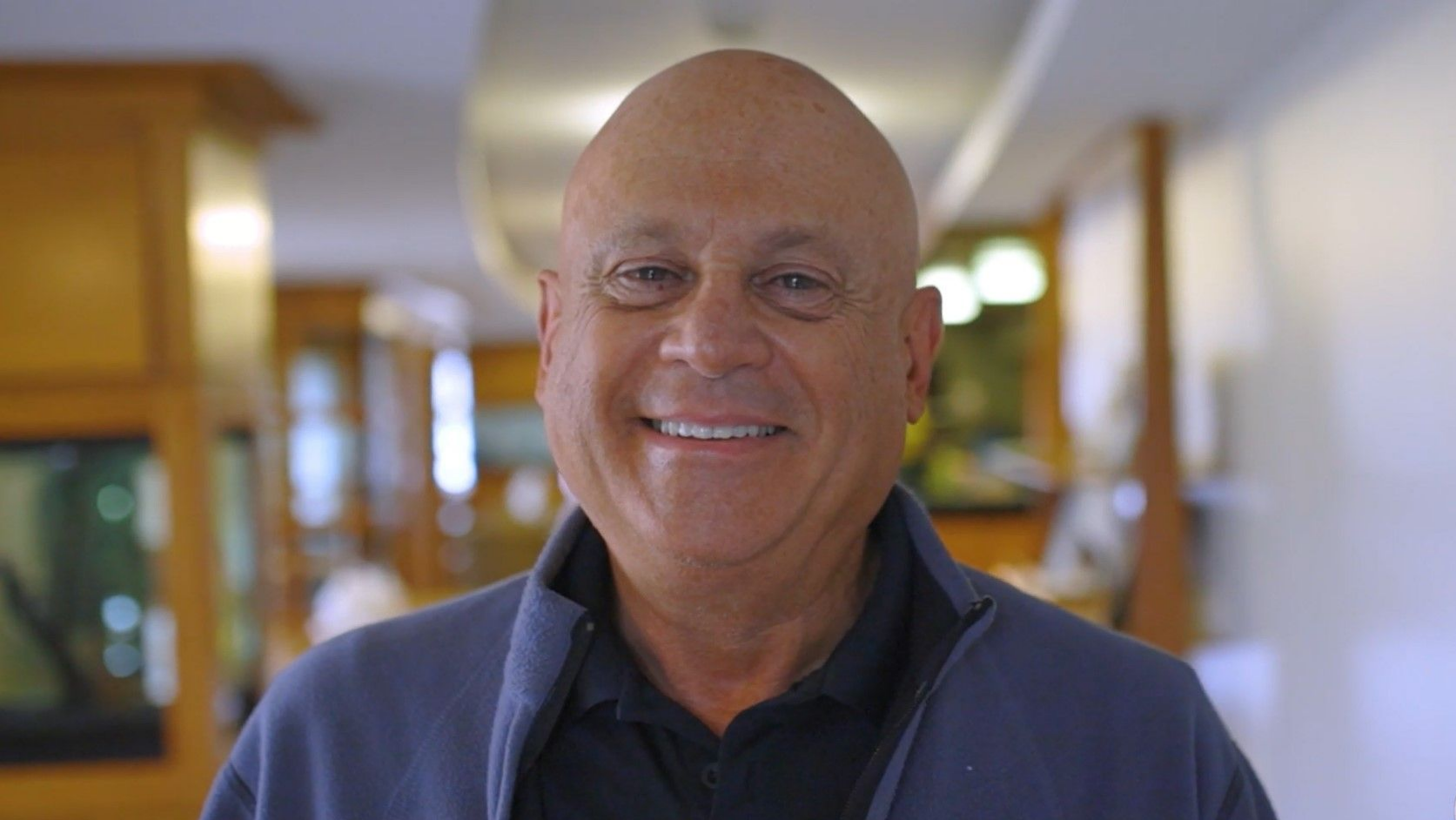 A bald man in a blue jacket is smiling for the camera.