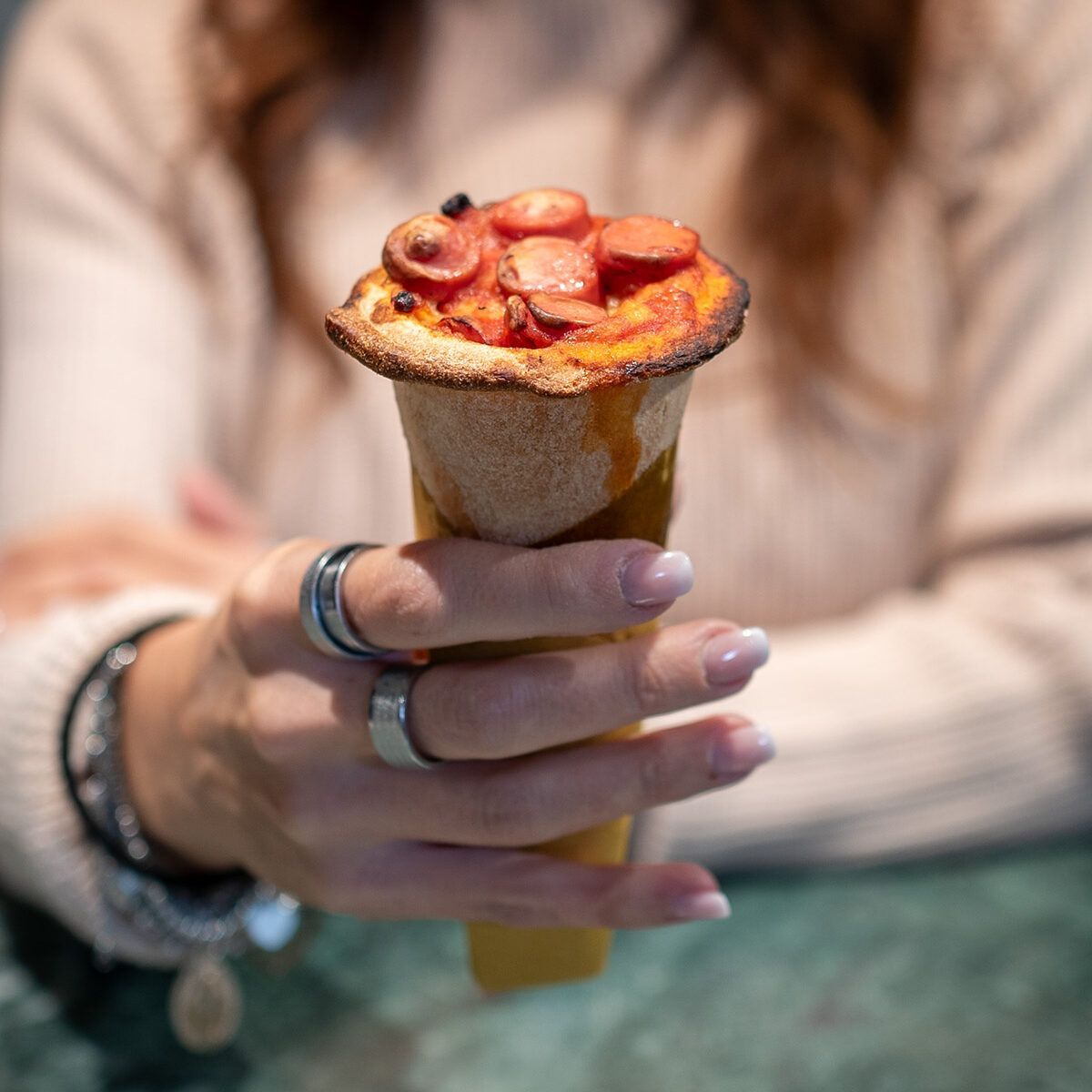 Mano che regge un cono di crêpe alla fragola guarnito con fragole a fette e salsa.
