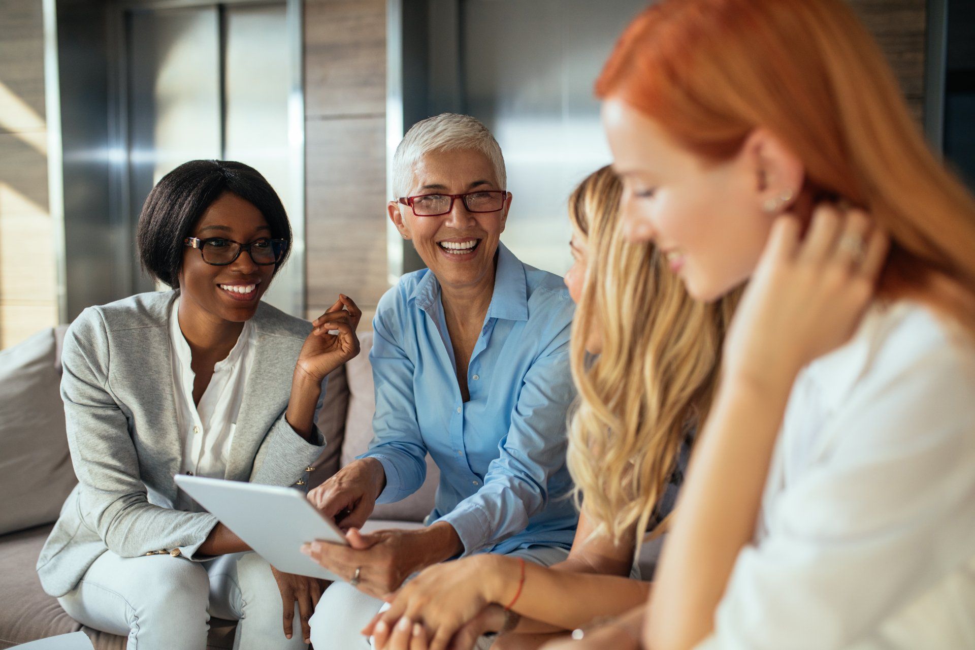 A group of women are sitting on a couch looking at a tablet.