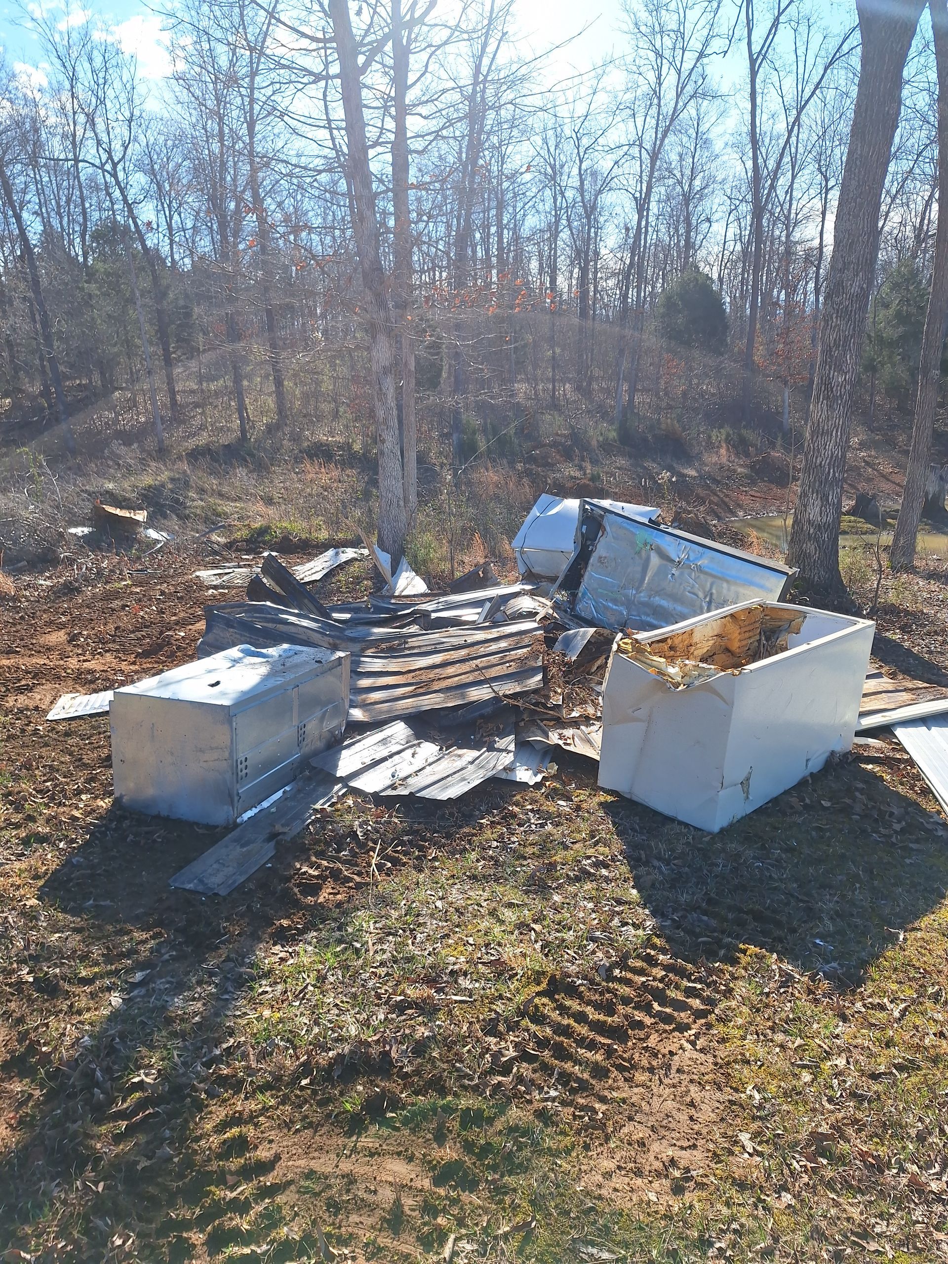 Burned outdoor debris pile with white appliances and charred wood in a wooded area