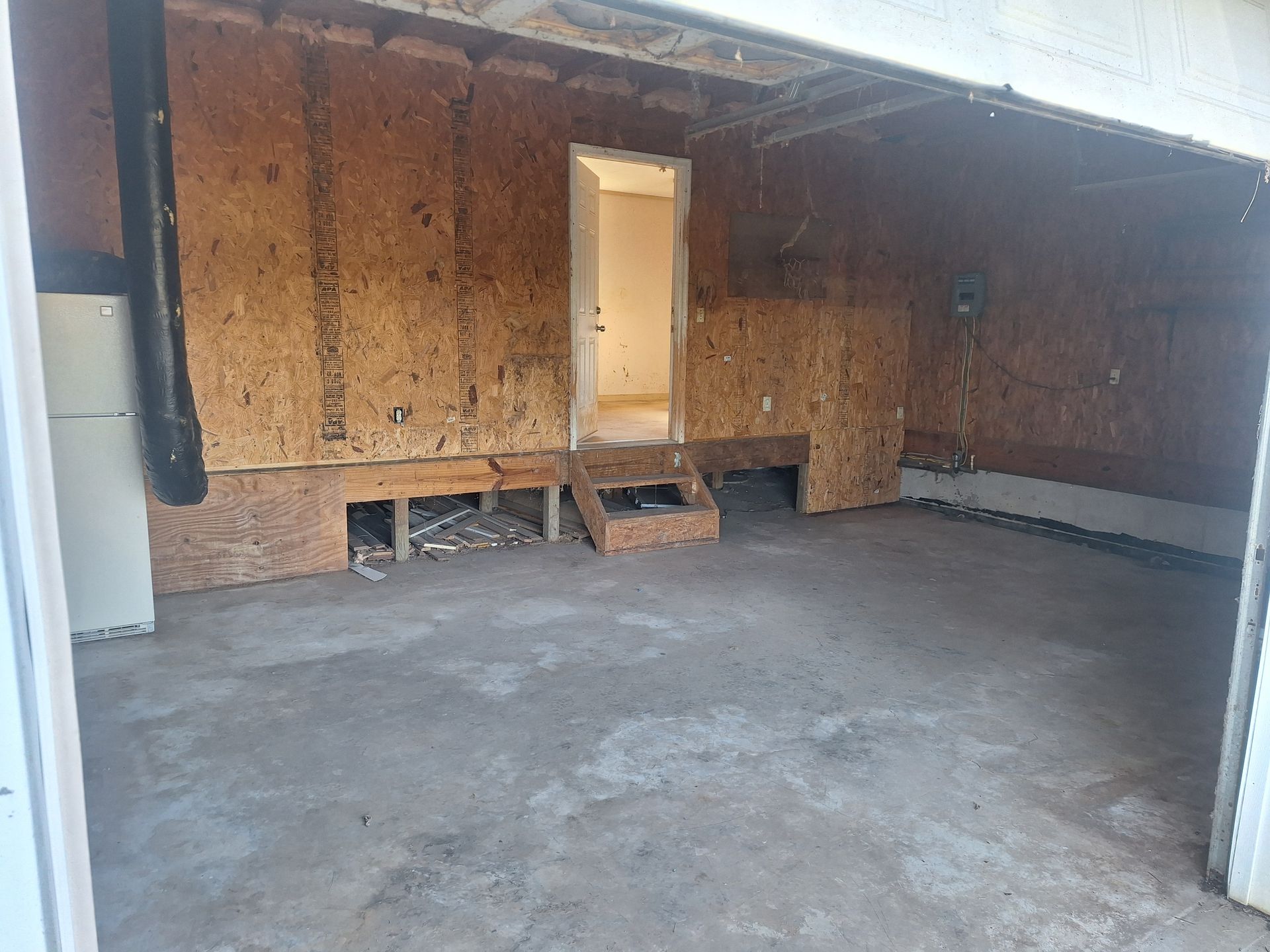 Empty garage under construction with exposed plywood walls and a concrete floor