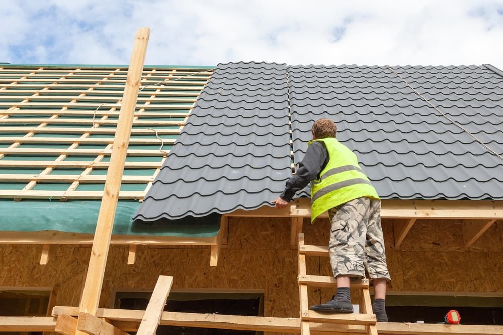 A Man is Standing on a Ladder Working on a Roof — Coastal Roofing Professionals In Byron Bay, NSW