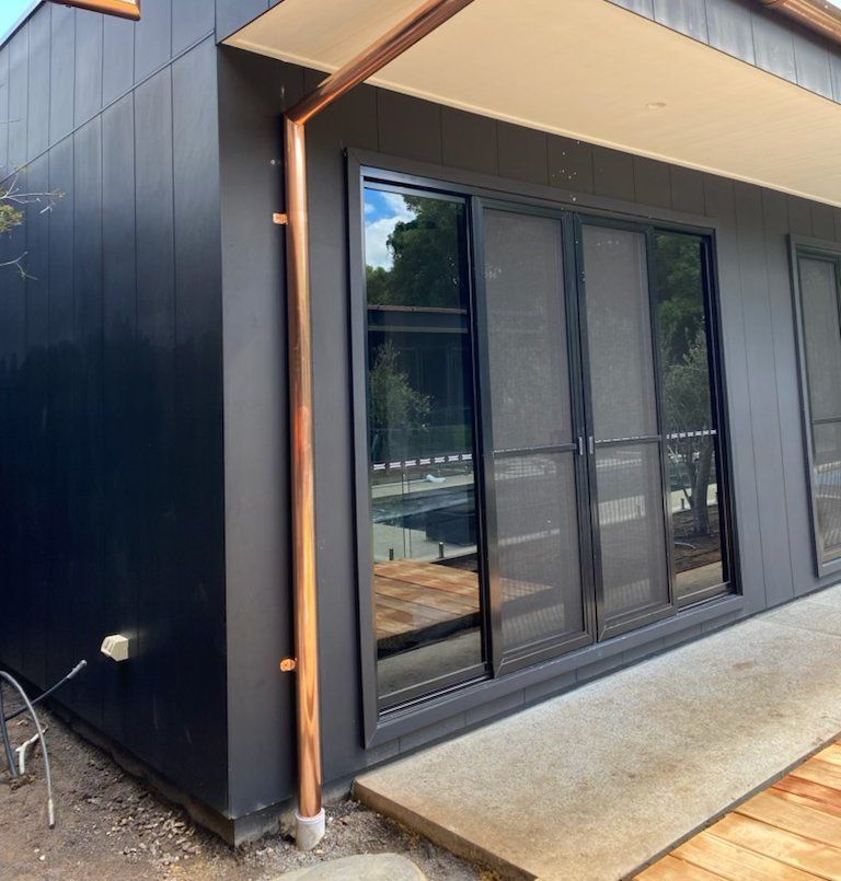 A Black House With a Copper Pipe on the Side — Coastal Roofing Professionals In Chinderah, NSW