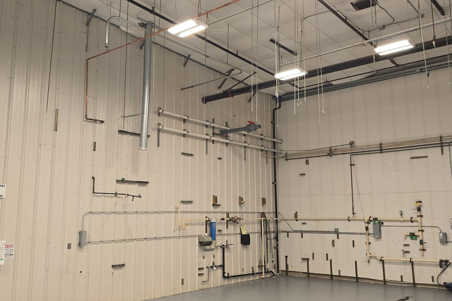 A large empty room with a lot of pipes hanging from the ceiling.
