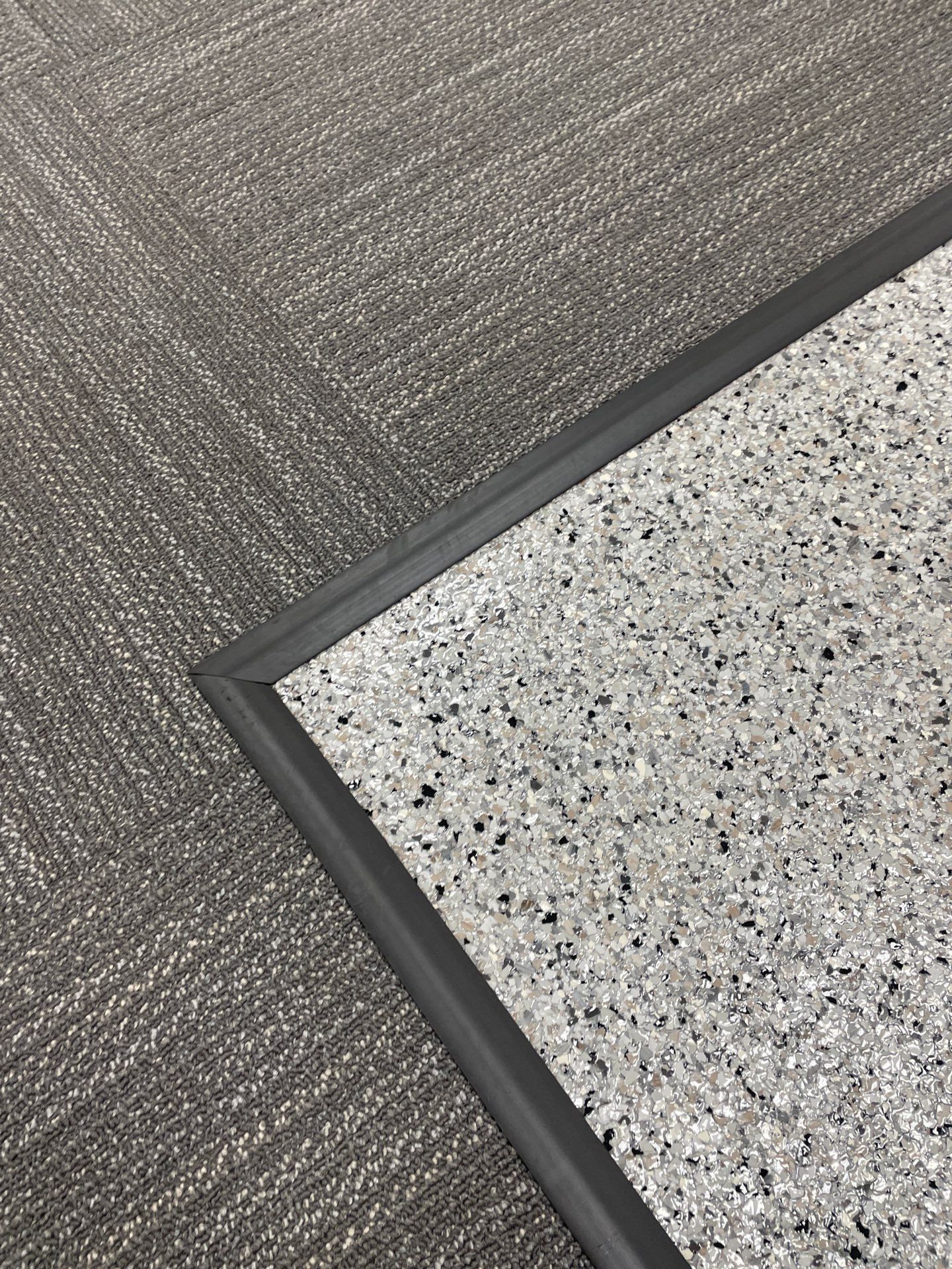 A close up of a rug on a carpeted floor with a black trim.