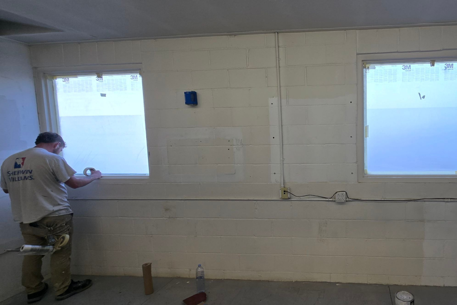A man is standing in a room with a brick wall and two windows.