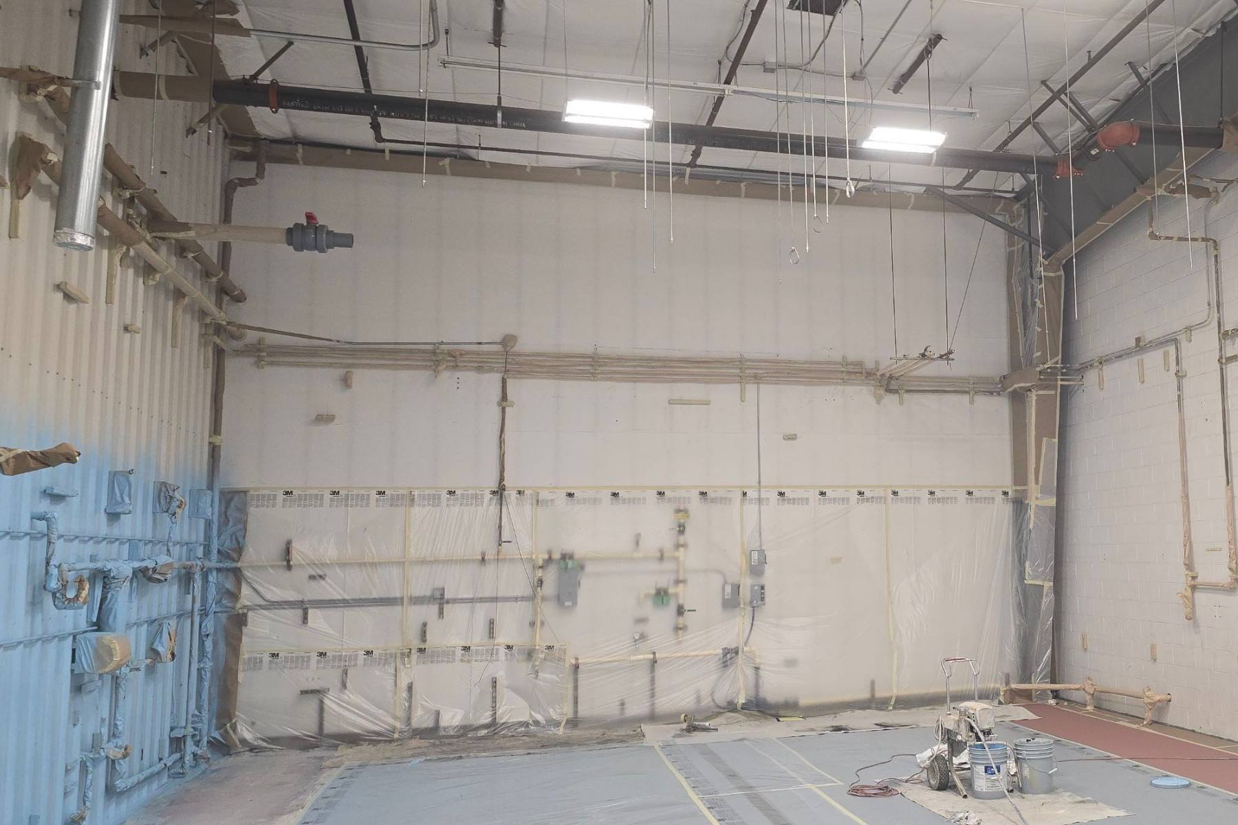 A large empty warehouse with a lot of pipes hanging from the ceiling.