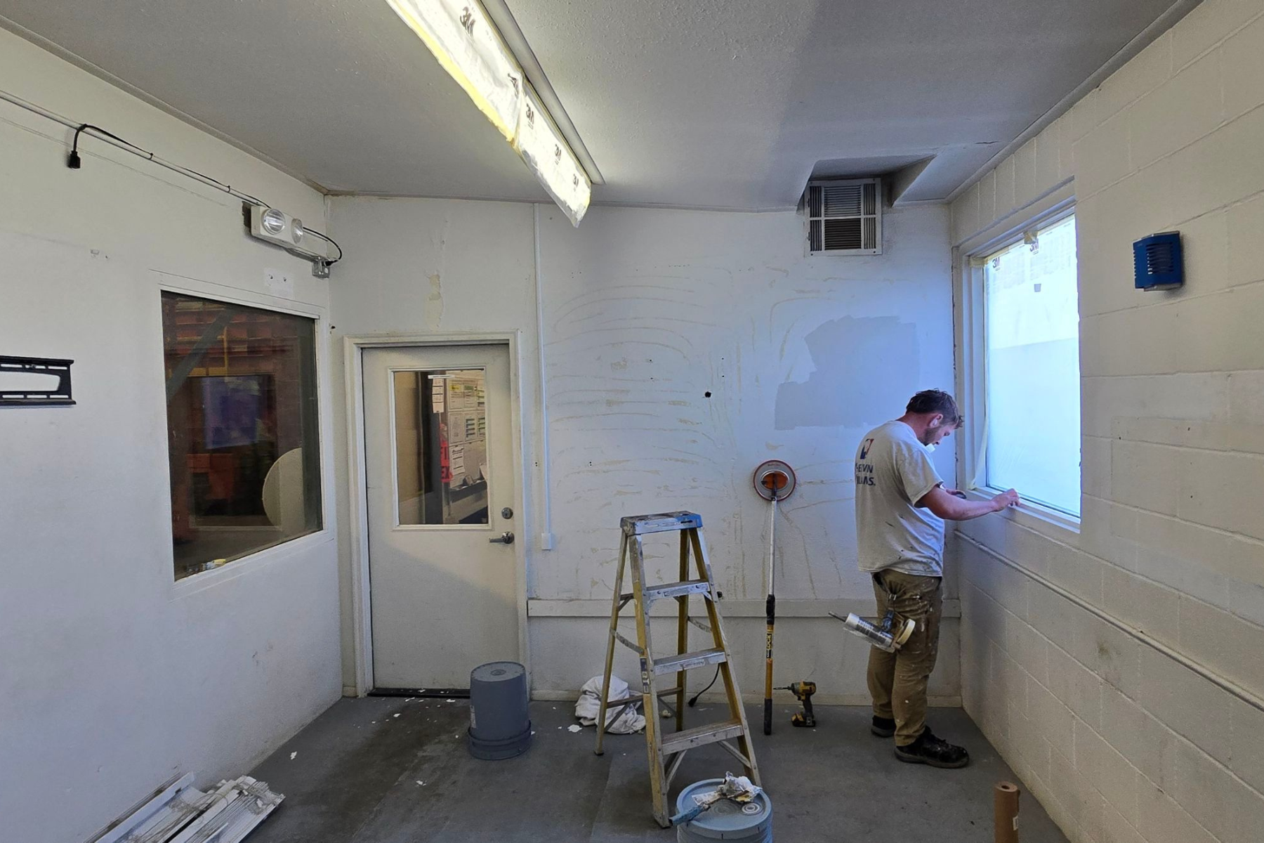 A man is measuring a window in a room with a ladder.