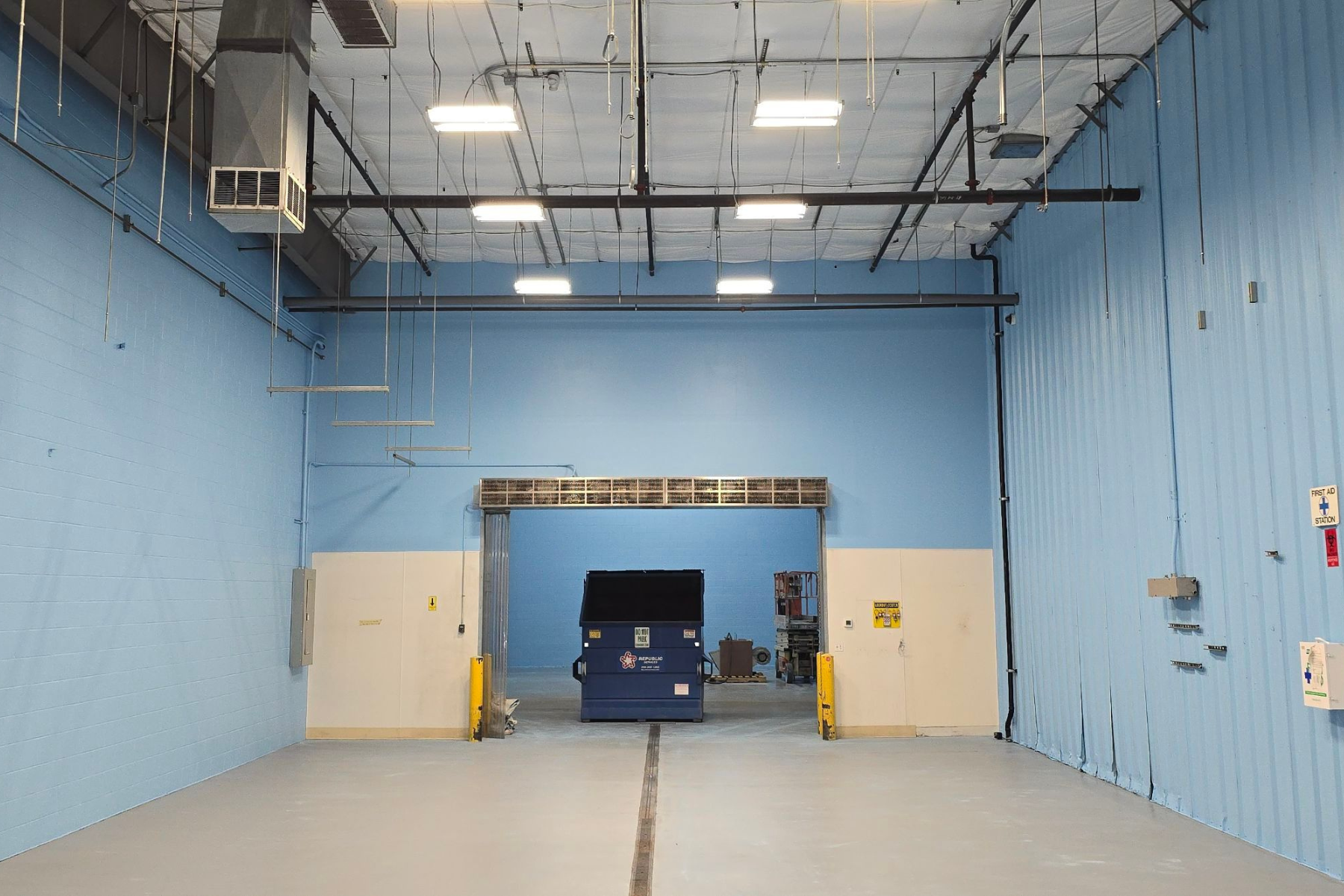 An empty warehouse with blue walls and a dumpster in the middle