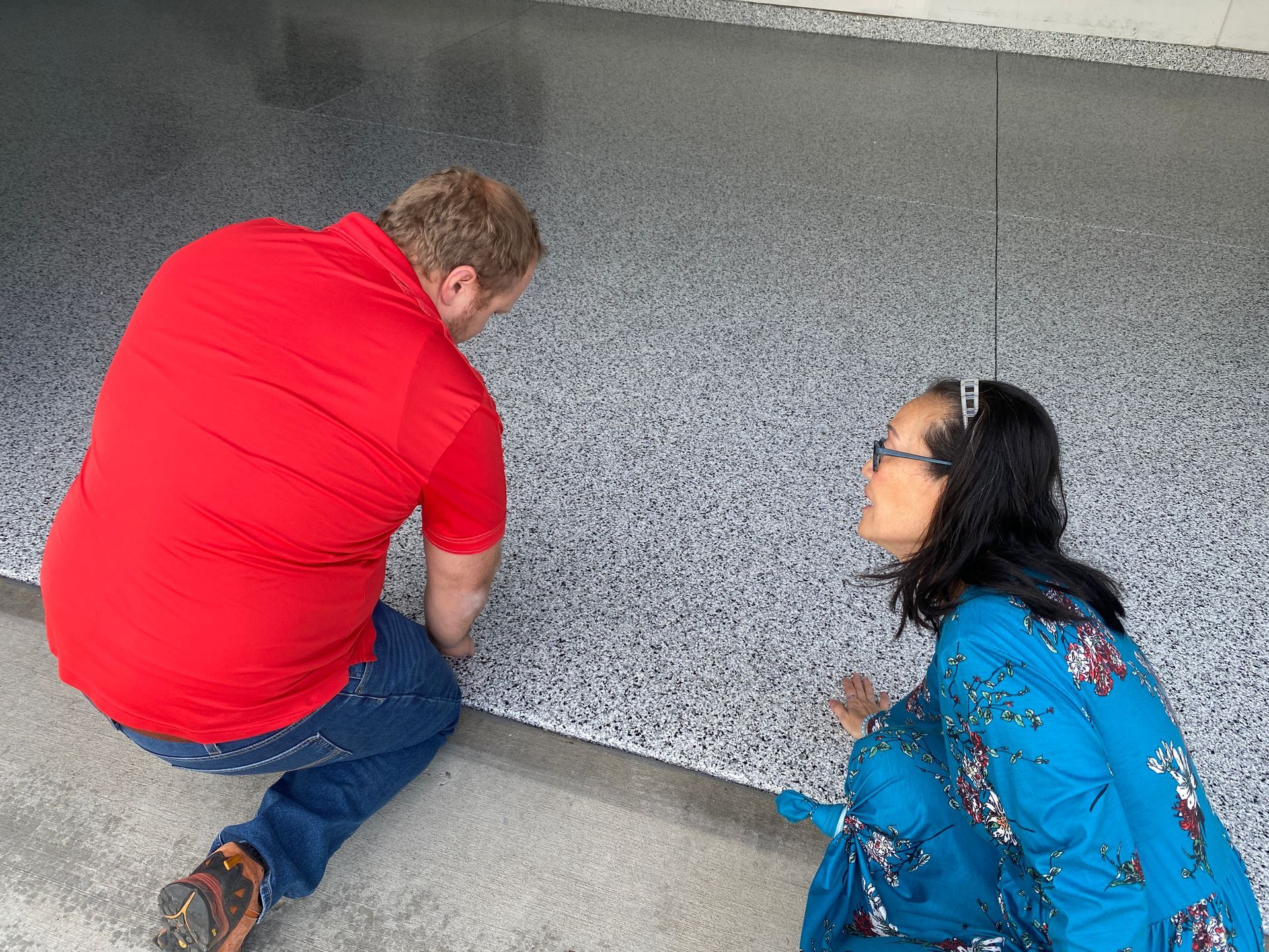 A man and a woman are kneeling down on a concrete floor.