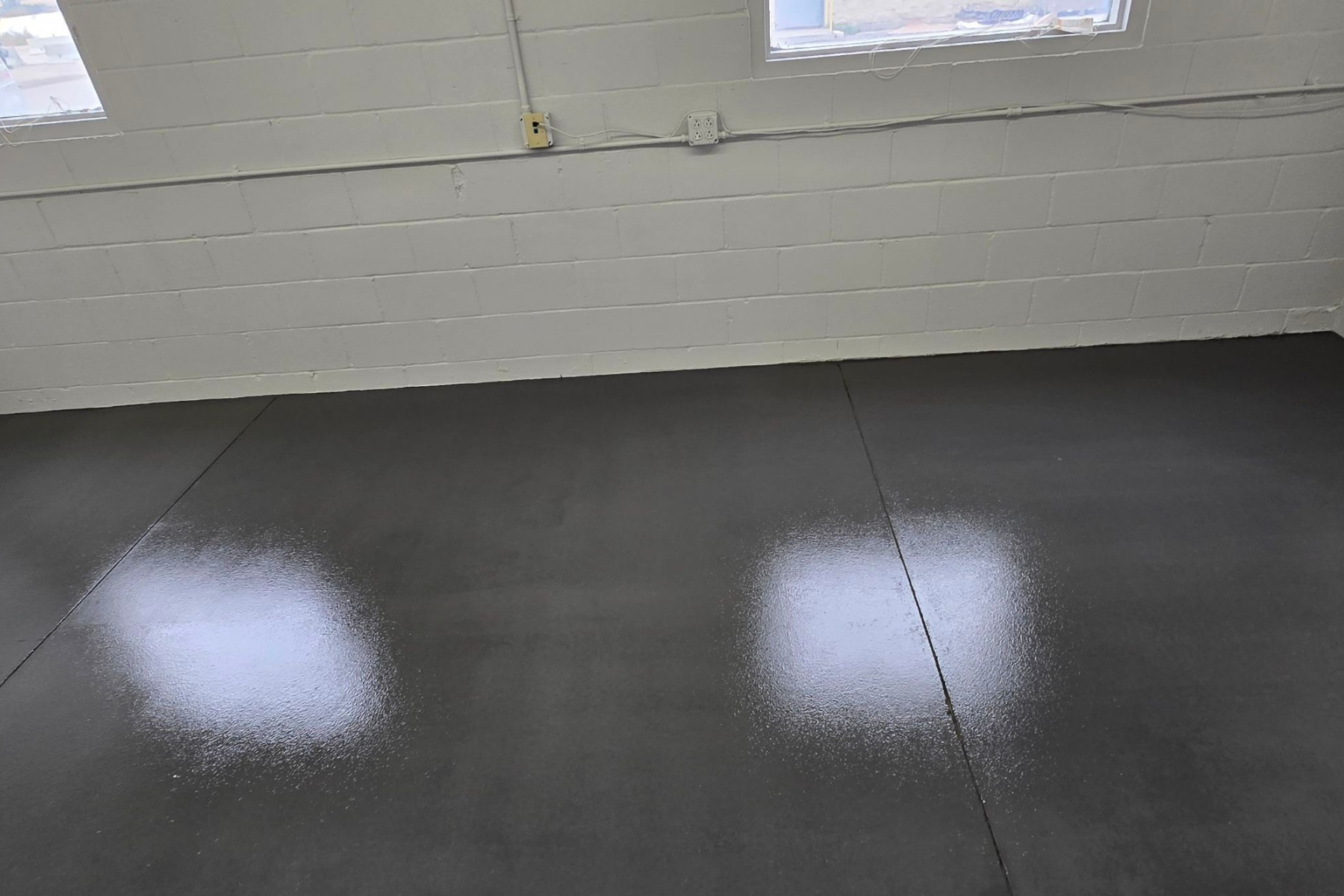 A black concrete floor with white spots on it in a room with white brick walls.