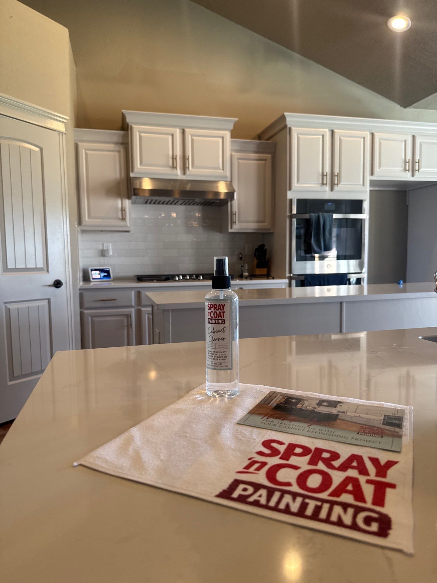 Kitchen interior with white cabinets and stainless appliances; spray paint can on a countertop beside a cloth.