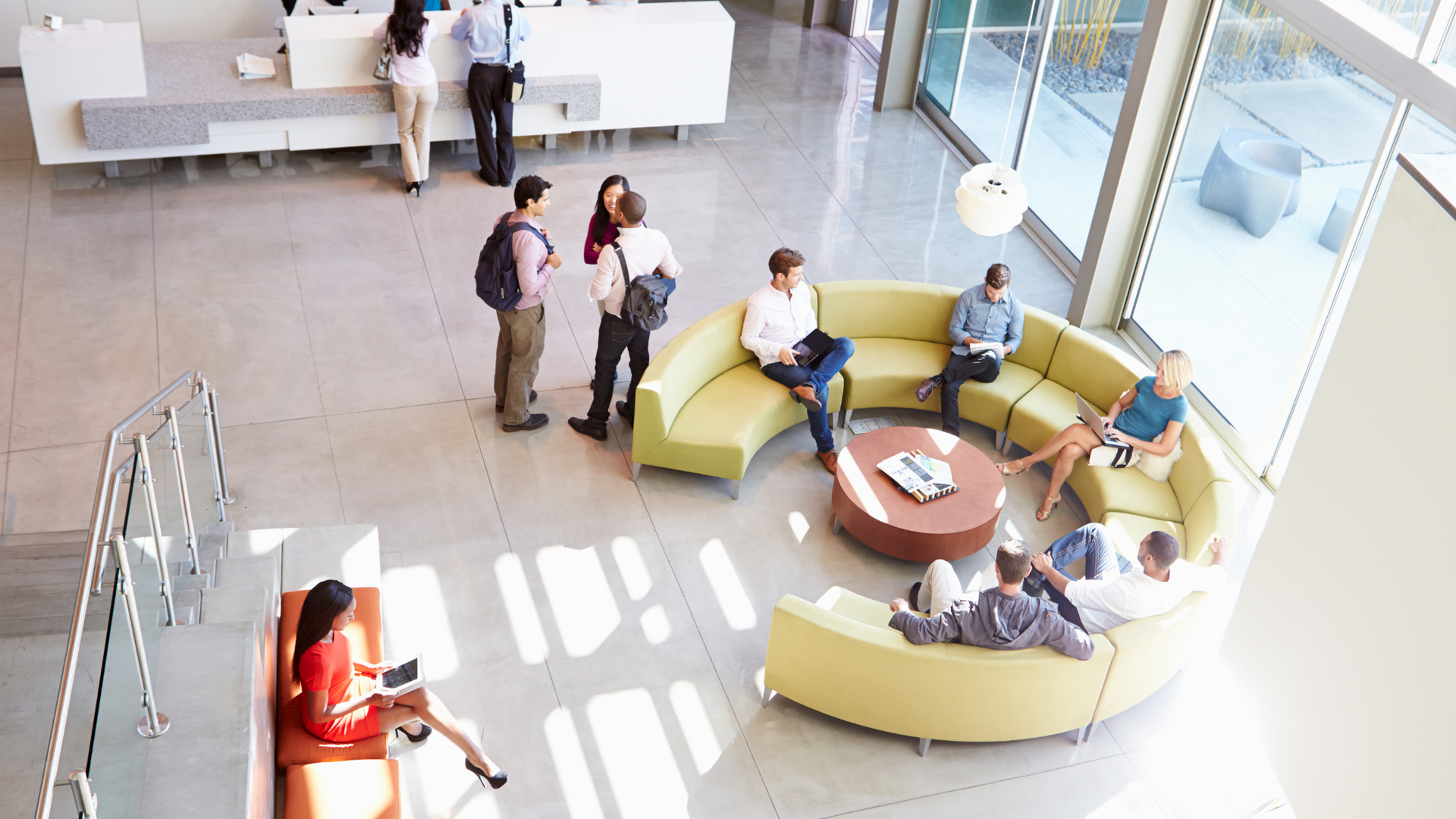 Modern office lobby with natural light, featuring seating areas, large windows, and people working.