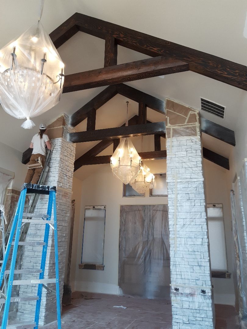 A man is standing on a ladder in a room with a chandelier hanging from the ceiling.