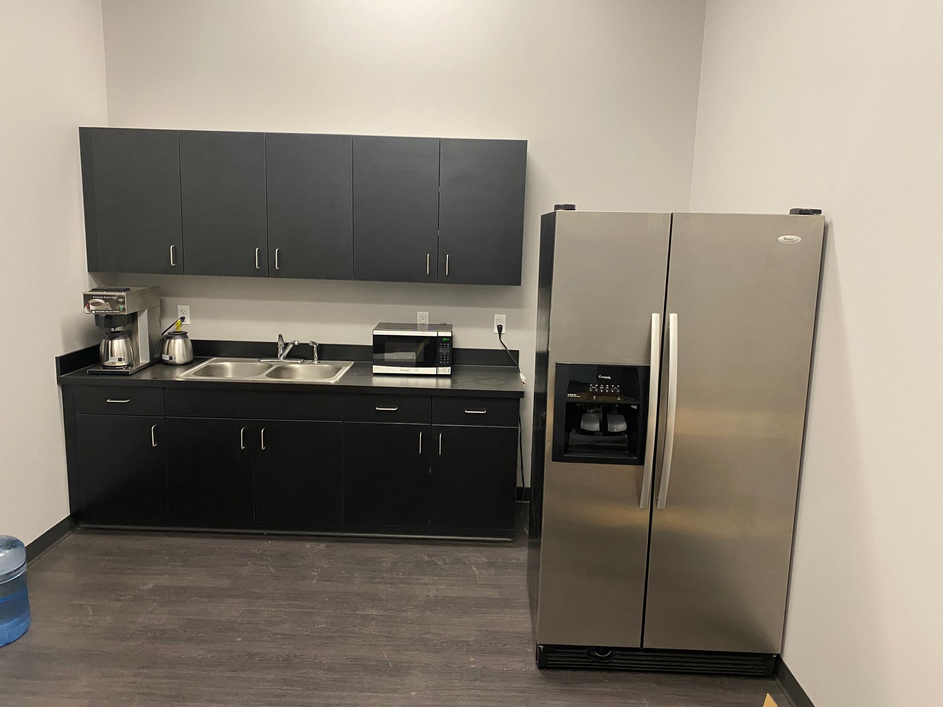 A kitchen with black cabinets and a stainless steel refrigerator