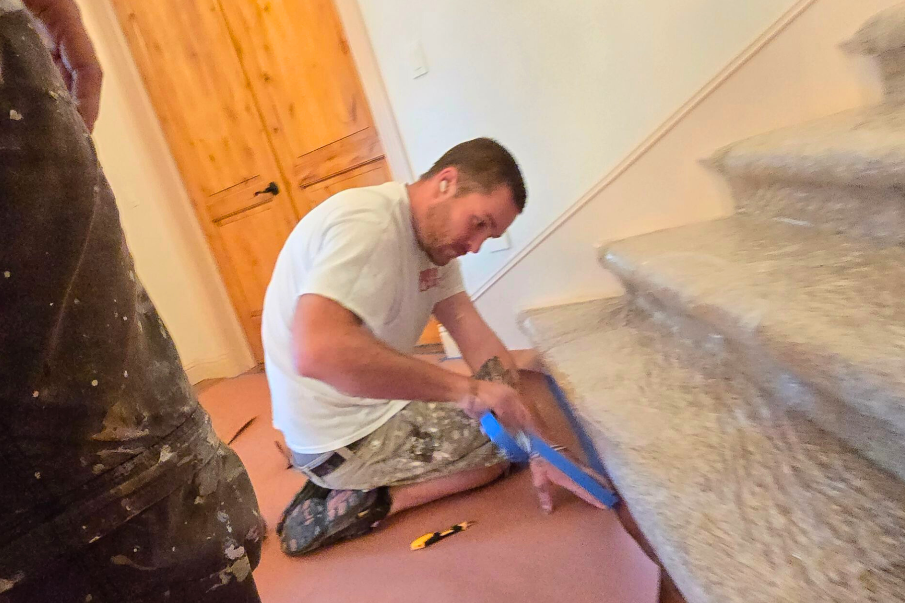 A man is kneeling down on the floor next to a set of stairs.