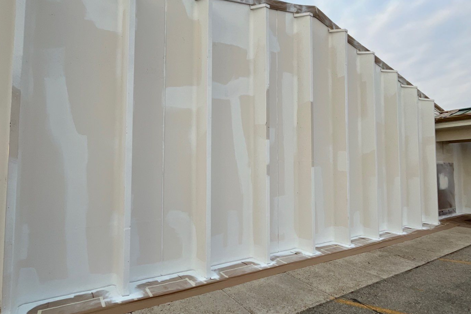 A large white wall is being painted in a parking lot.