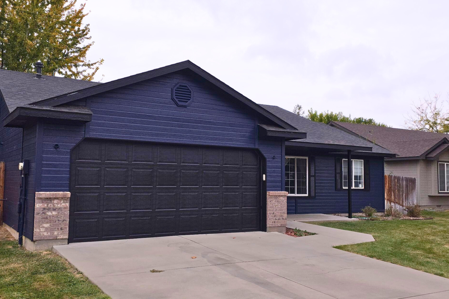 A blue house with a black garage door and a driveway.