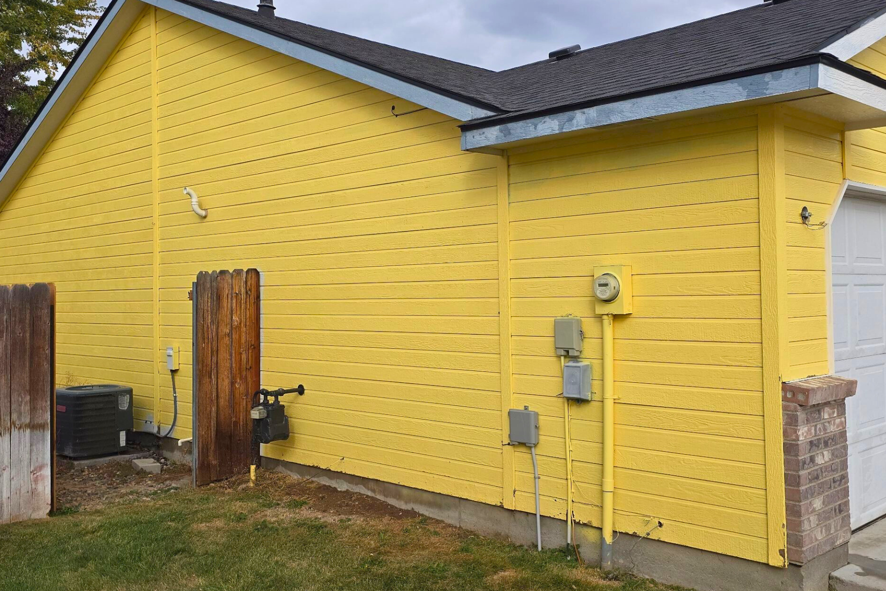 The side of a yellow house with a garage and a fence.