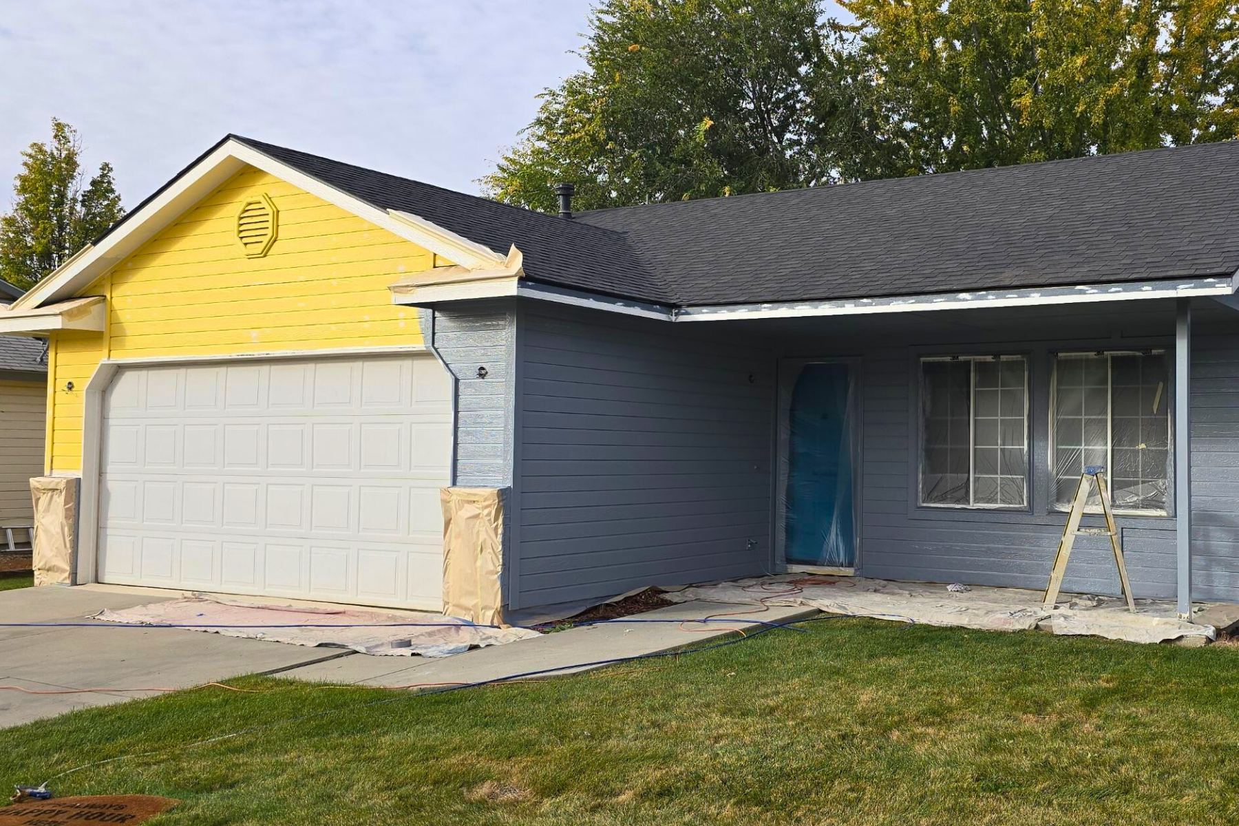 A blue house with a yellow siding is being painted.