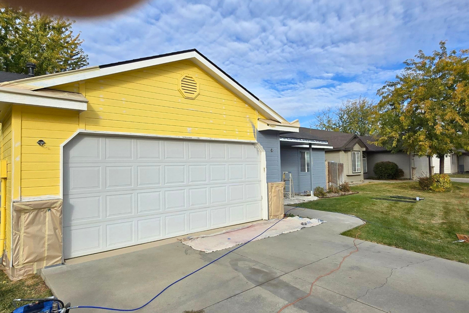 A yellow house with a white garage door is being painted.